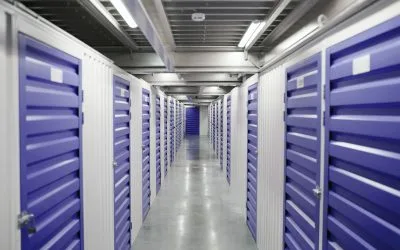 Clean, indoor self-storage facility hallway lined with secure green metal units. Affordable and reliable storage services in Sharjah by dubaicitymovers.ae.
